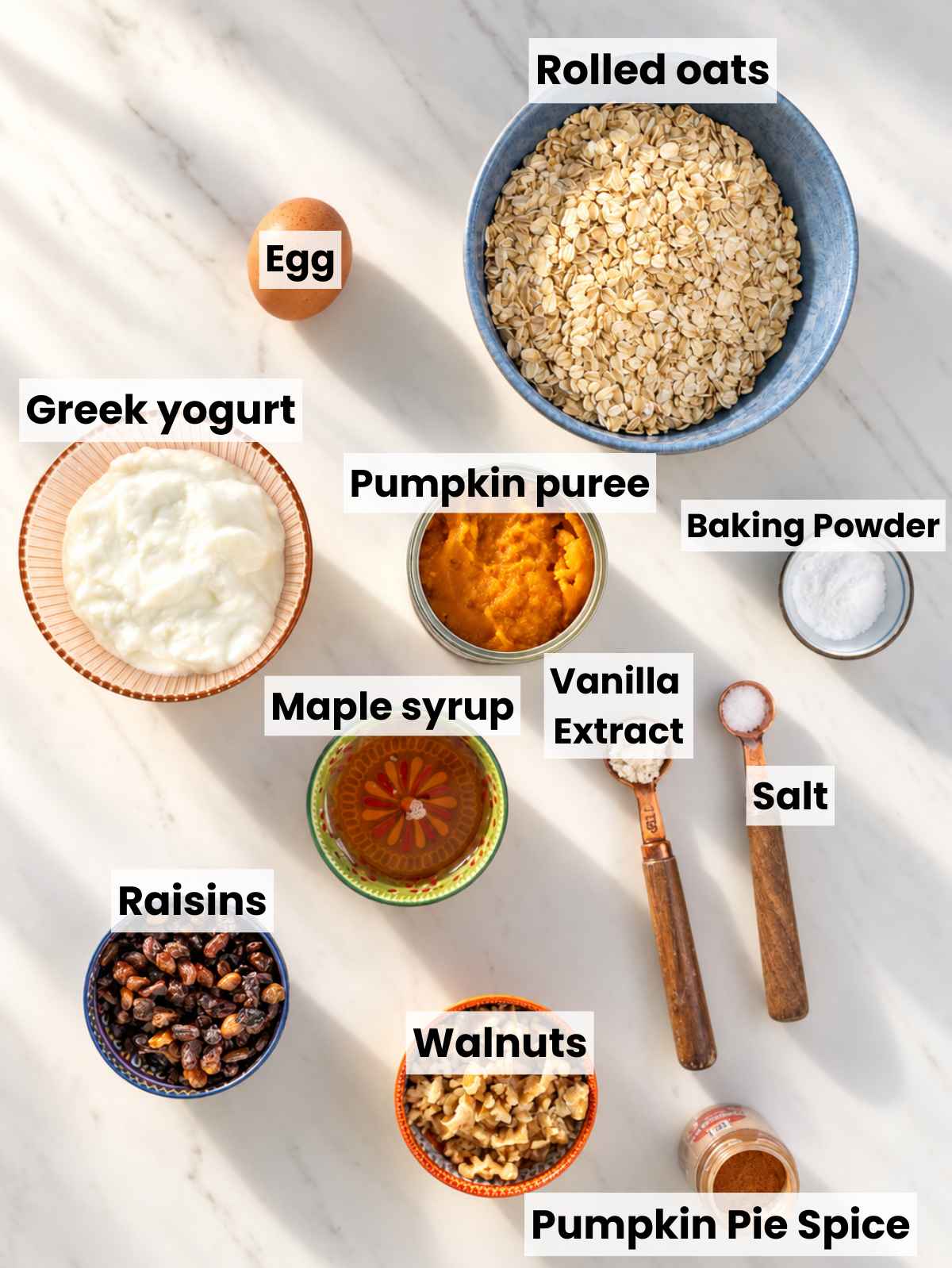 Pumpkin puree, oats, Greek yogurt, maple syrup, egg, raisins, walnuts, and spices on marble.
