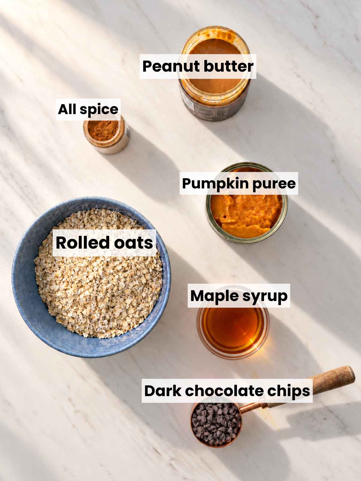 Pumpkin pureฬe, oats, peanut butter, maple syrup, spices, and chocolate chips on marble.