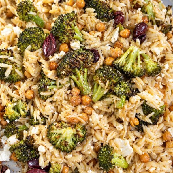 Sheet pan roasted broccoli orzo with chickpeas, olives, and feta in bright natural light.