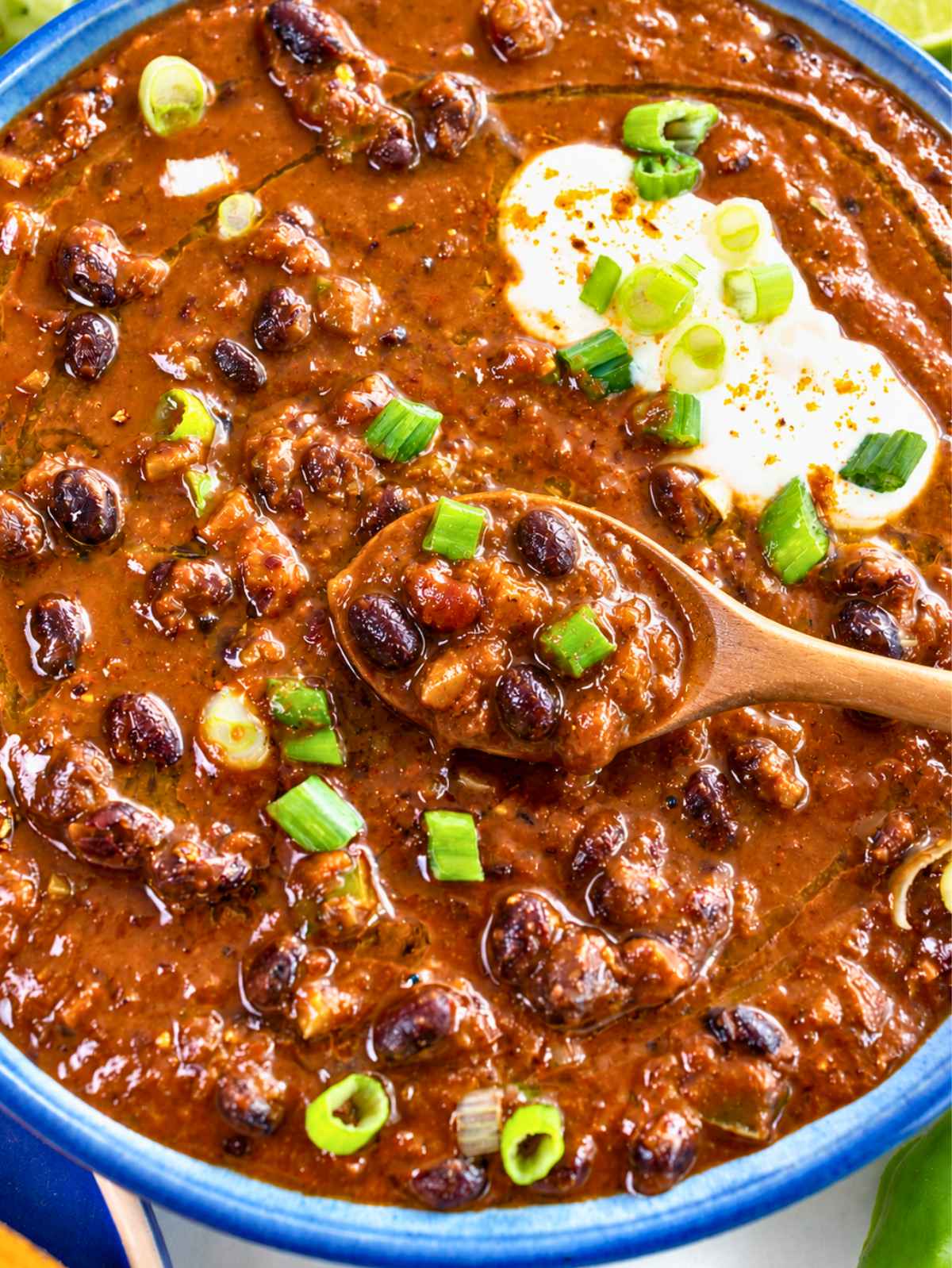 Spoon resting in a bowl of thick Cajun black bean soup with green onions.