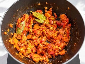 Step 2 Garlic, tomato paste, bay leaves, oregano, and pepper flakes coating softened vegetables.