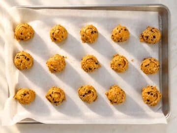 Step 3 Rounded scoops of pumpkin cookie dough spaced across a parchment-lined baking sheet.