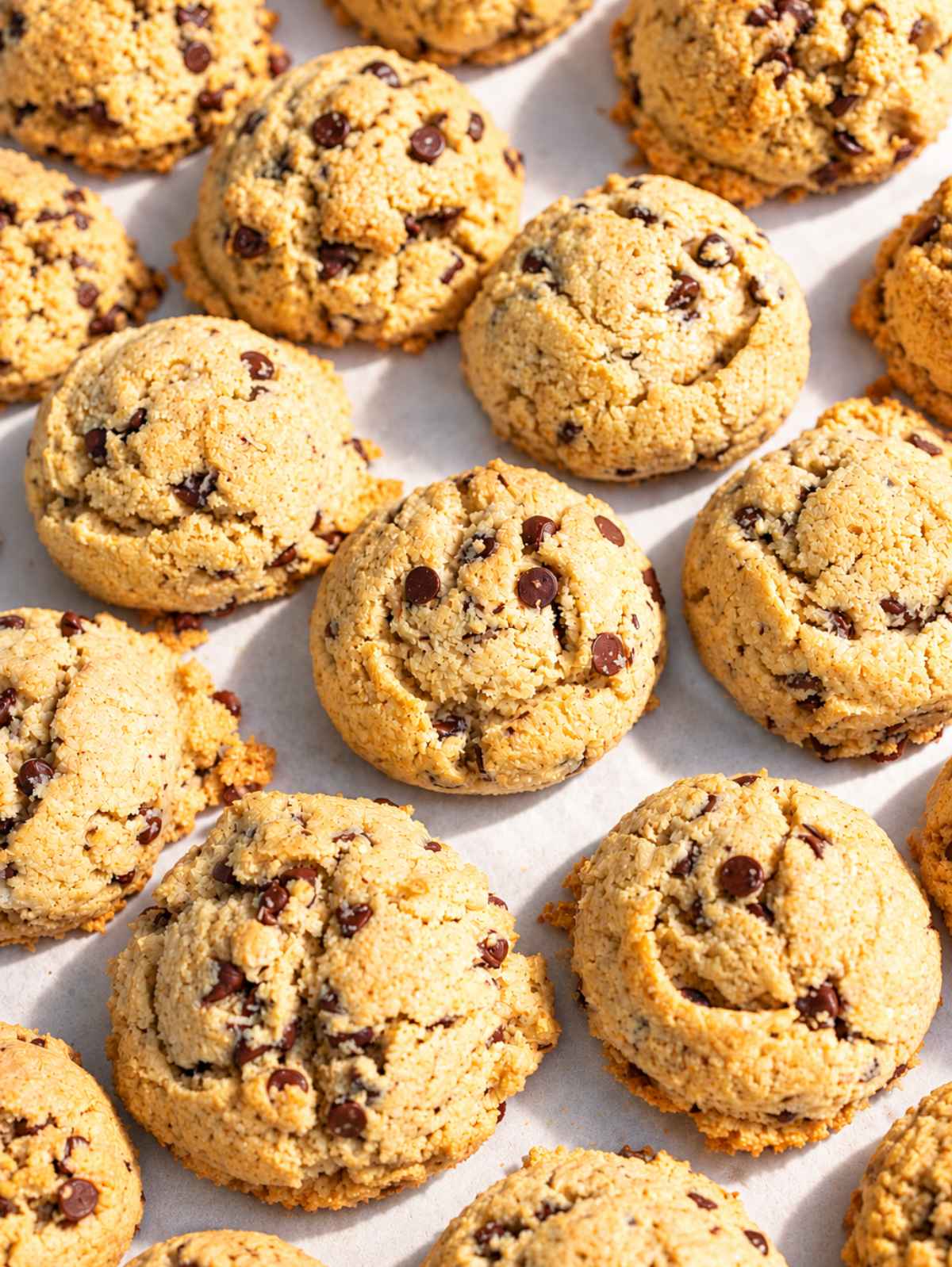Thick almond flour chocolate chip cookies arranged side by side on a white marble table, showing their rustic golden tops.